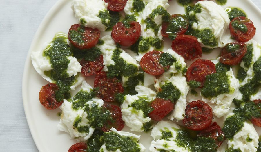 Roasted cherry tomatoes and pieces of mozzarella on a plate, drizzled with basil purée